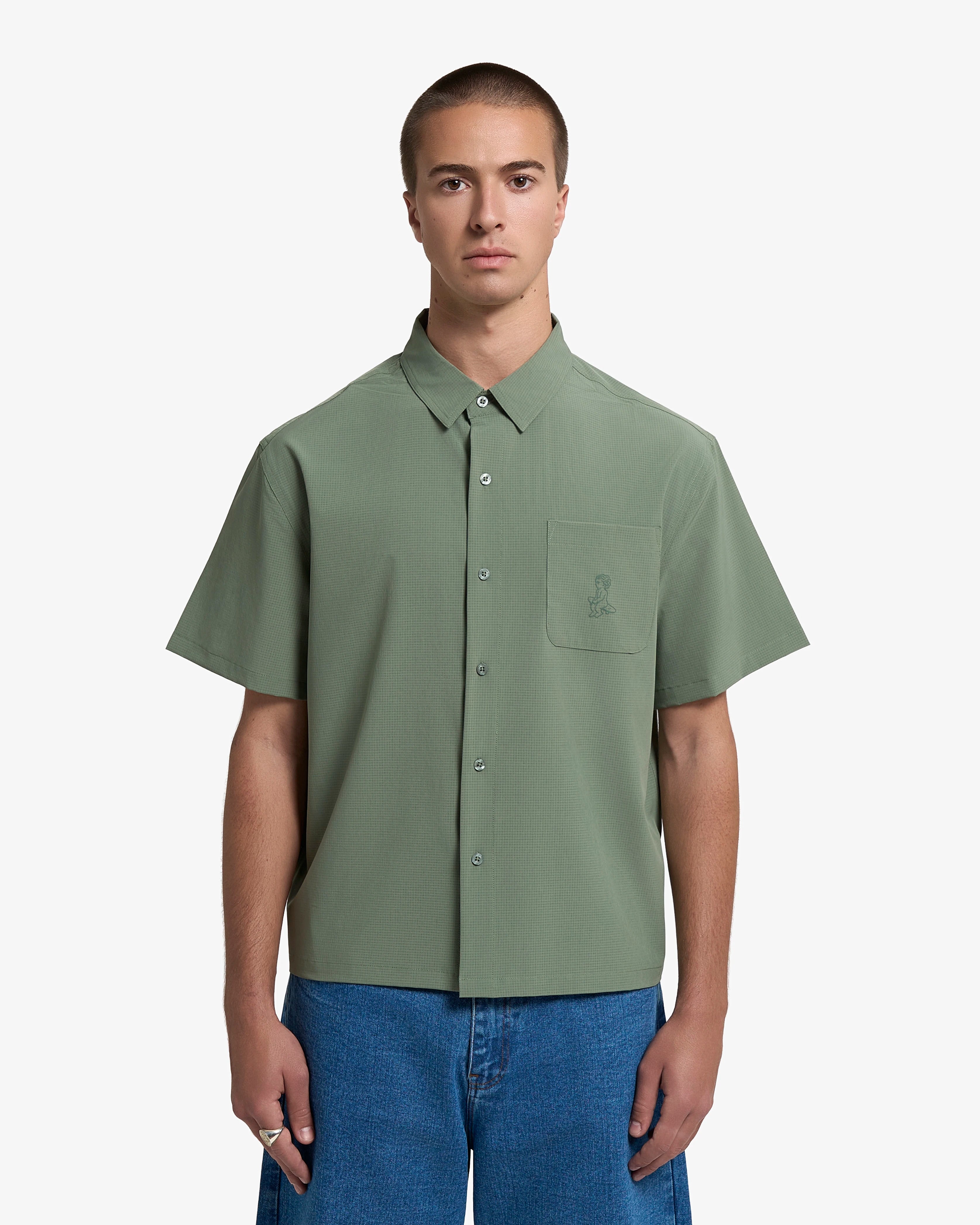 Short sleeve button-up shirt designed for everyday wear
Lightweight textured fabric with a subtle grid structure and dry hand feel
Boxy fit with a straight, slightly cropped silhouette
Front button closure with a chest pocket
Ikon logo printed on the front pocket
Green colour with a tonal finish