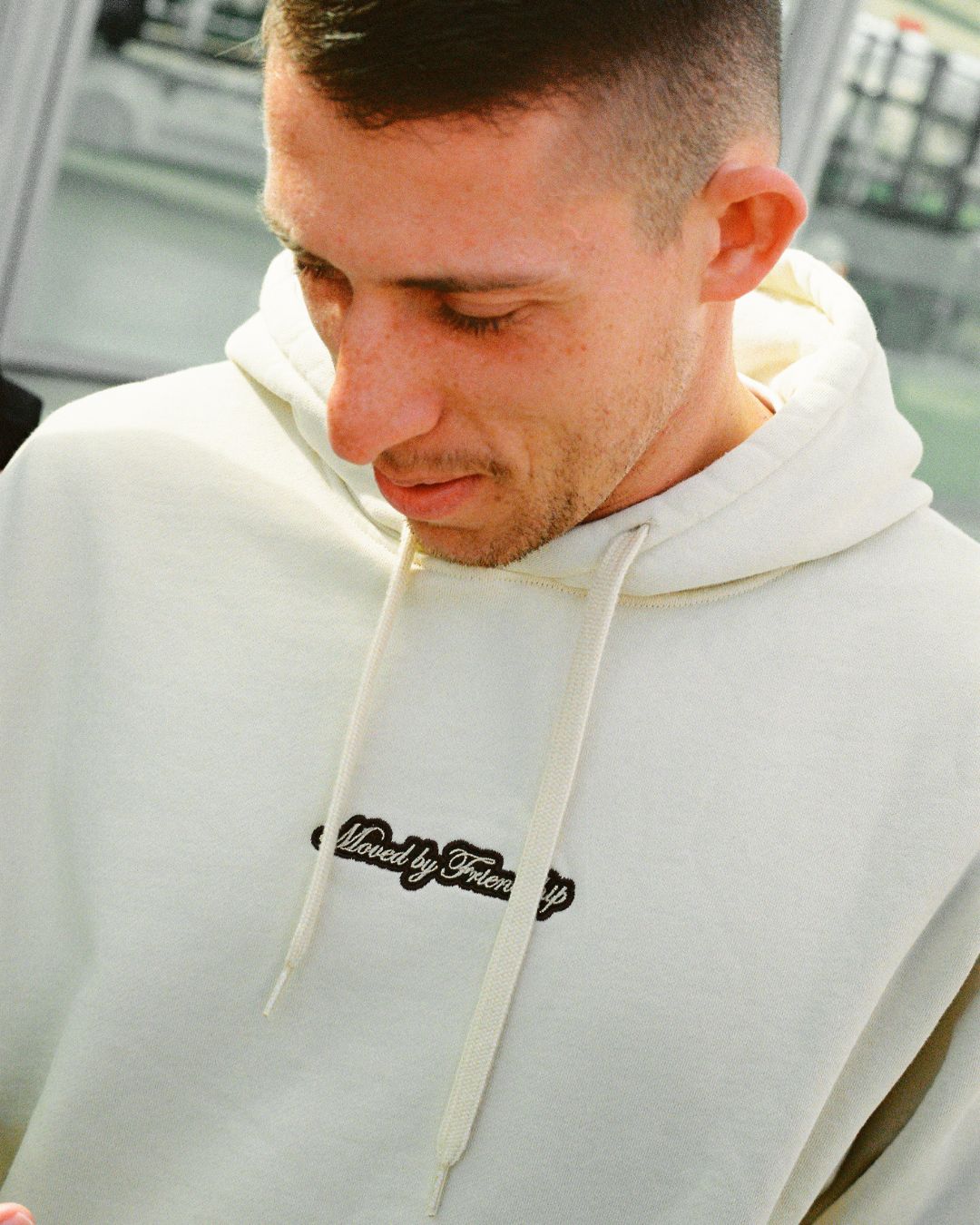 The Friendship Hoodie in off-white features the motto "Moved By Friendship" embroidered on the front in a classic handwritten style. On the back, the Ikon logo appears with a dragged effect, adding a distinctive detail.
