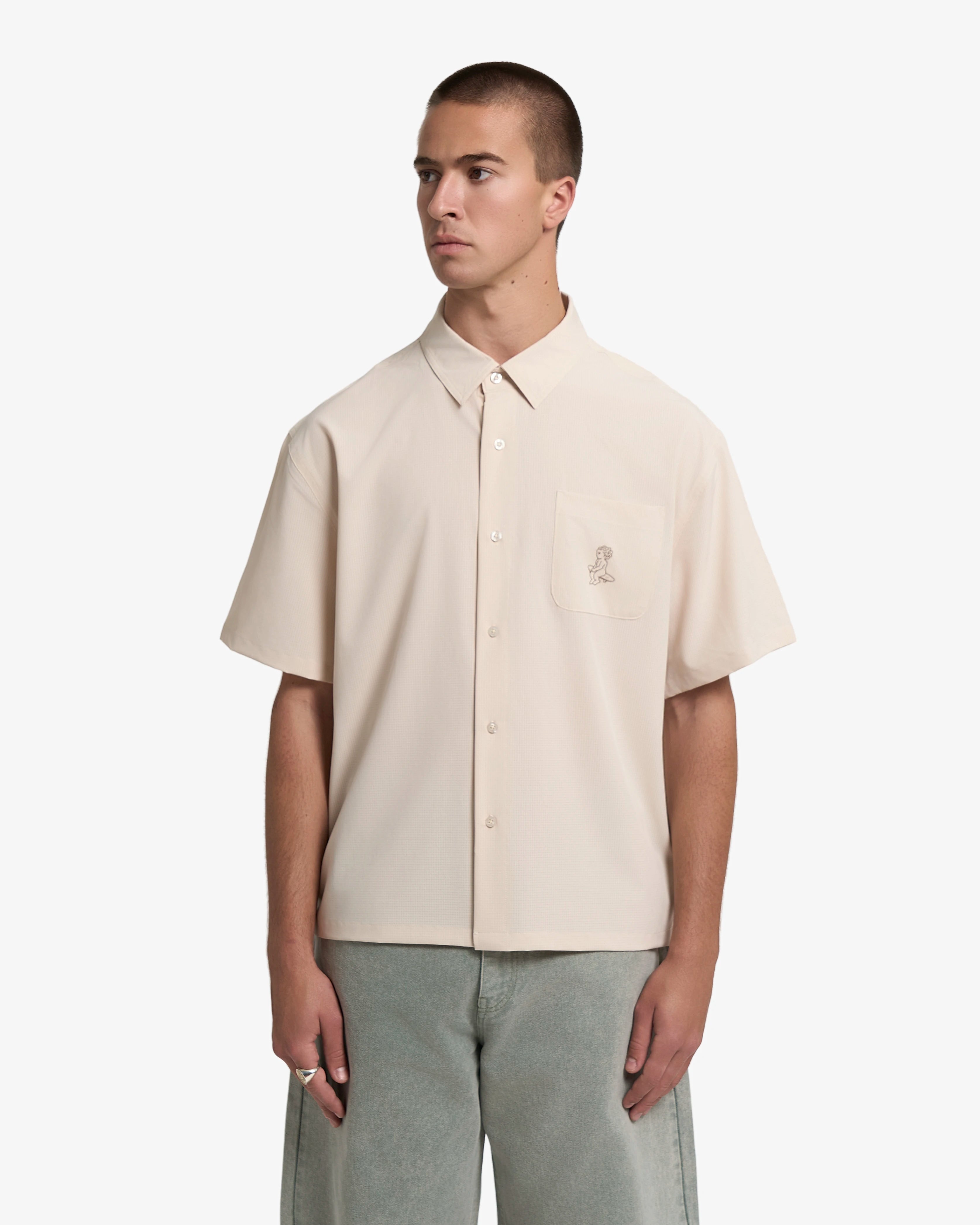 Short sleeve button-up shirt designed for everyday wear
Lightweight textured fabric with a subtle grid structure and dry hand feel
Boxy fit with a straight, slightly cropped silhouette
Front button closure with a chest pocket
Ikon logo printed on the front pocket
Sand colour with a tonal finish